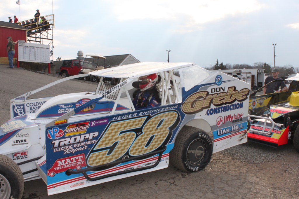 A dirt car driver is sitting inside his car and is waiting for the start of the hot laps