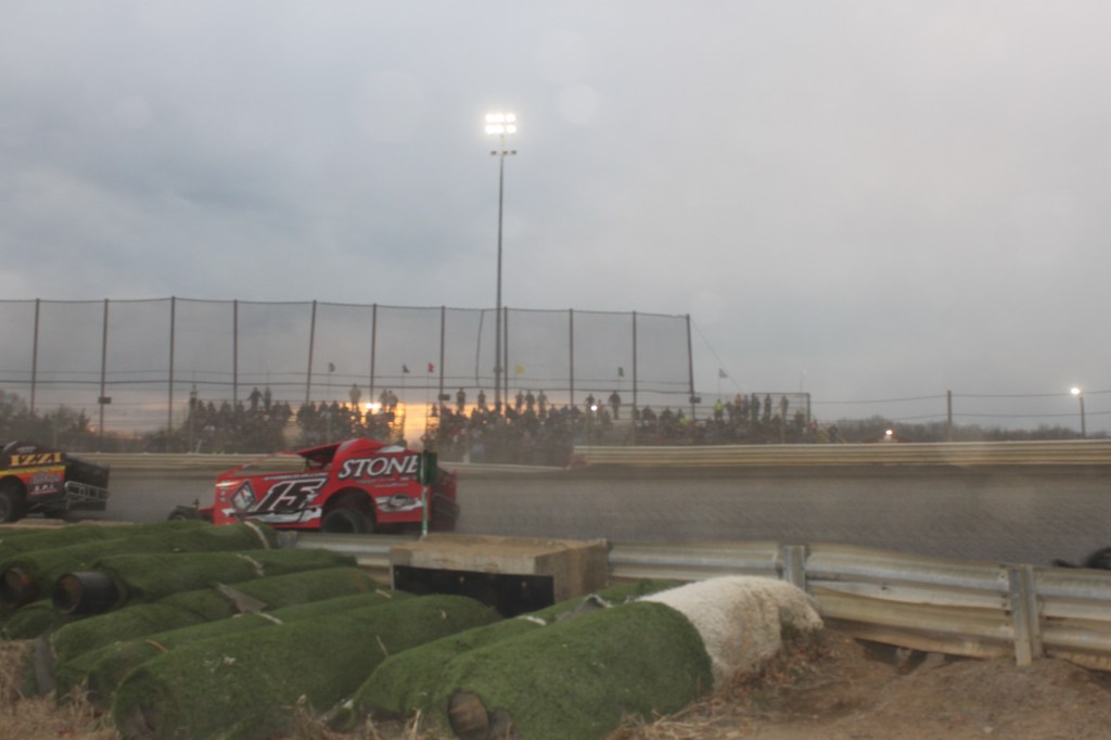 A dirt car is cornering at the speedway track. The grandstand may also be seen.